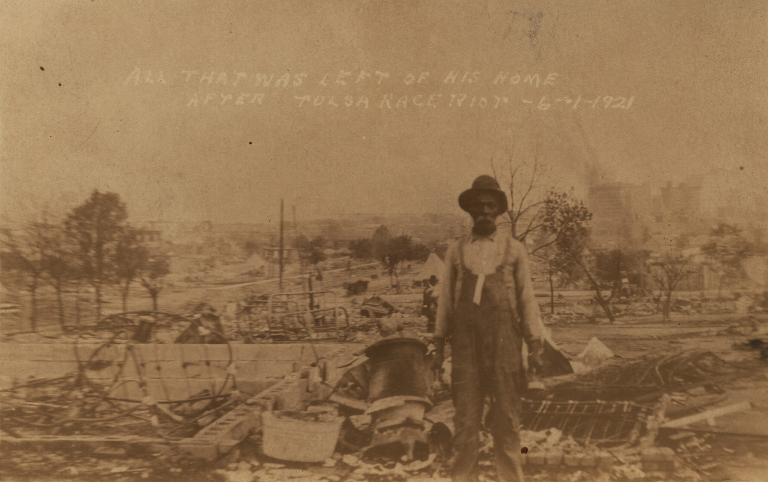 A postcard showing an unidentified man standing alone amidst the desolation and the ruins of what is described as his home. The placement of the ruins of Dunbar Elementary School in the background indicates that this photo was taken on either North Greenwood Ave. or North Frankfort Ave.