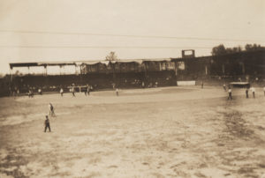 Photographic print of McNulty baseball park at 11th and Elgin. People are walking across the outfield and through the diamond. Buildings visible in the background.