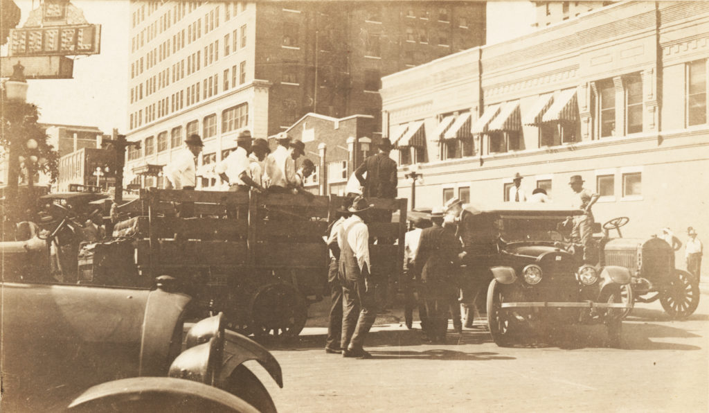 A photographic print showing men being loaded on a truck. The photo was taken at 2nd St. looking down Cincinnati Ave. towards the Hotel Tulsa