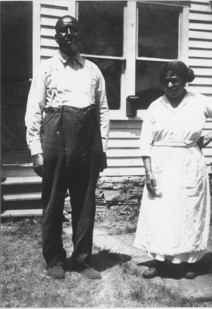 An older man and woman are standing outside a house. Provenance is unknown; however, it is believed that these photos were taken in Tulsa prior to the Race Riot.