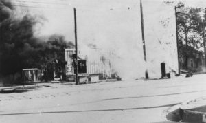 A photographic reproduction of a photo taken of an unidentified grocery being burned. Based on the "[Fre]sh [Groce]ries" sign in the window, the style of building, and the tracks running along the street, this may be Friedman Bros. Groceries at 301 Archer St. "G3 of 28" written on back.