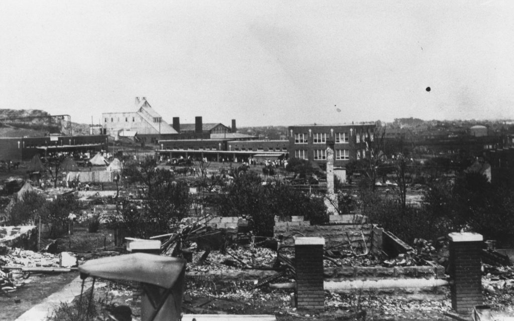 A photographic reproduction of a photo taken looking over the ruins of 507 N. Detroit at Booker T. Washington High School. Tulsa Pressed Brick Co. off to the left. Title supplied by cataloger. "G13 of 28" written on back.