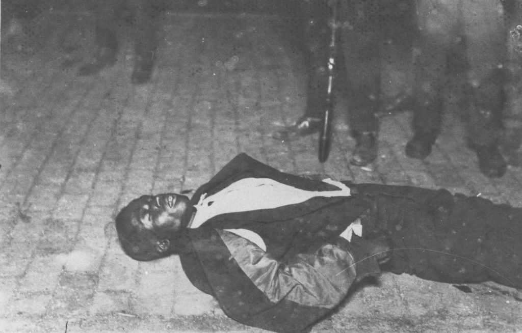 A photographic reproduction of a photo taken of dead man was lying on a brick paved street at night. He was likely killed in the early part of the riot, the evening of 31 May, or early in the morning of the 1st. "G18 of 28" written on back. Title written on back.