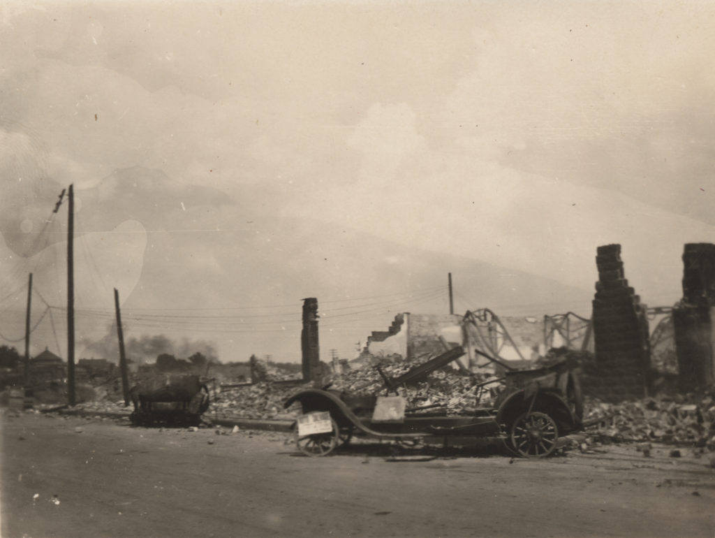 Image of a burnt out car and the residental area behind it.